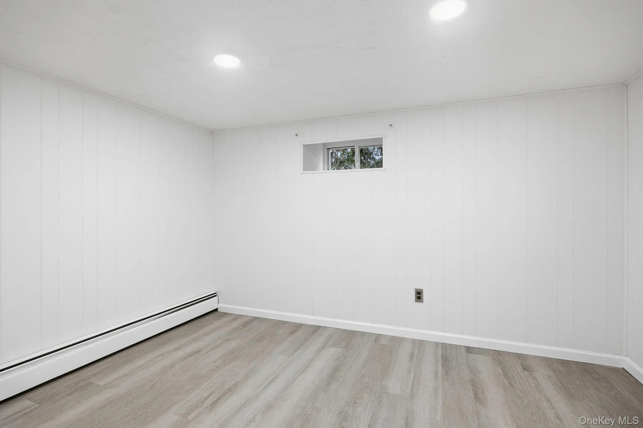 Empty room with a baseboard heating unit, light wood-style floors, recessed lighting, and wooden walls Empty room with a baseboard heating unit, light wood-style floors, recessed lighting, and wooden walls