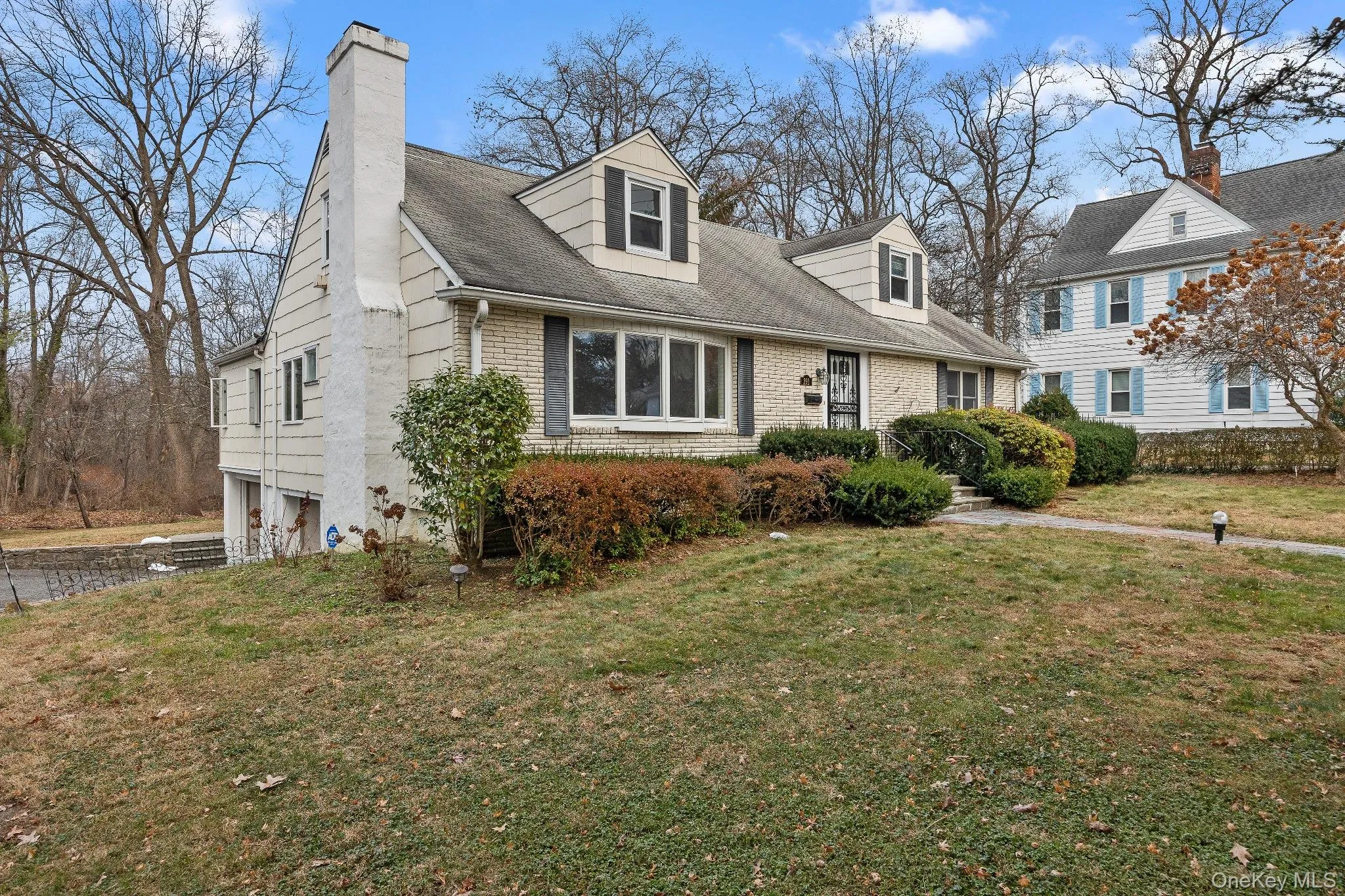 Cape cod home with a front lawn, brick siding, a chimney, and roof with shingles Cape cod home with a front lawn, brick siding, a chimney, and roof with shingles