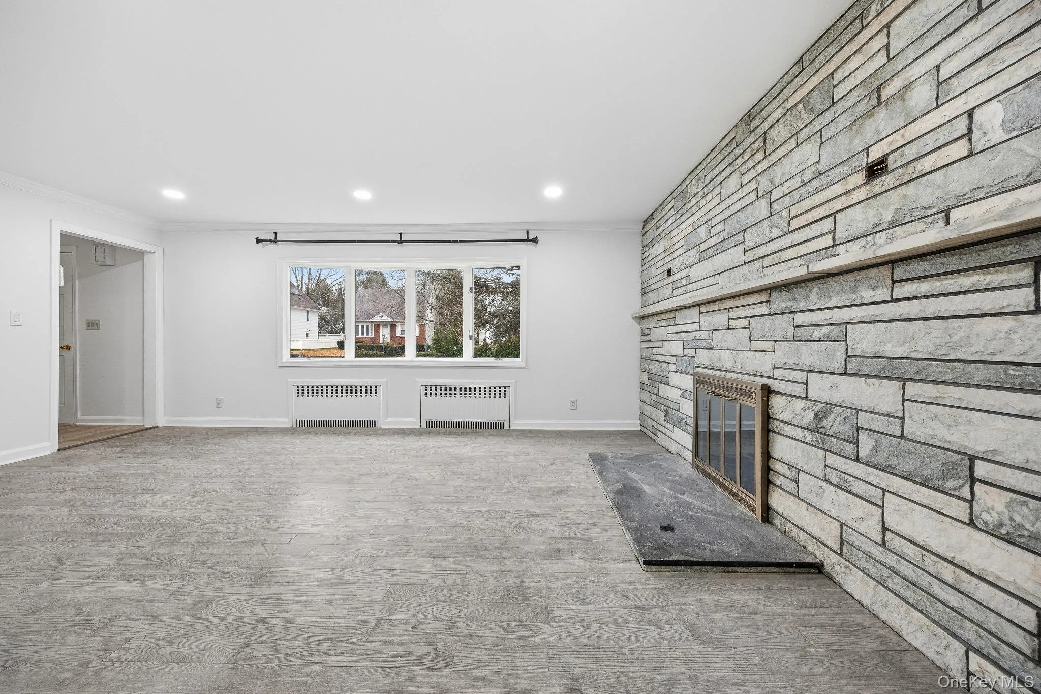 Unfurnished living room featuring a fireplace, radiator heating unit, ornamental molding, light wood-style flooring, and recessed lighting Unfurnished living room featuring a fireplace, radiator heating unit, ornamental molding, light wood-style flooring, and recessed lighting