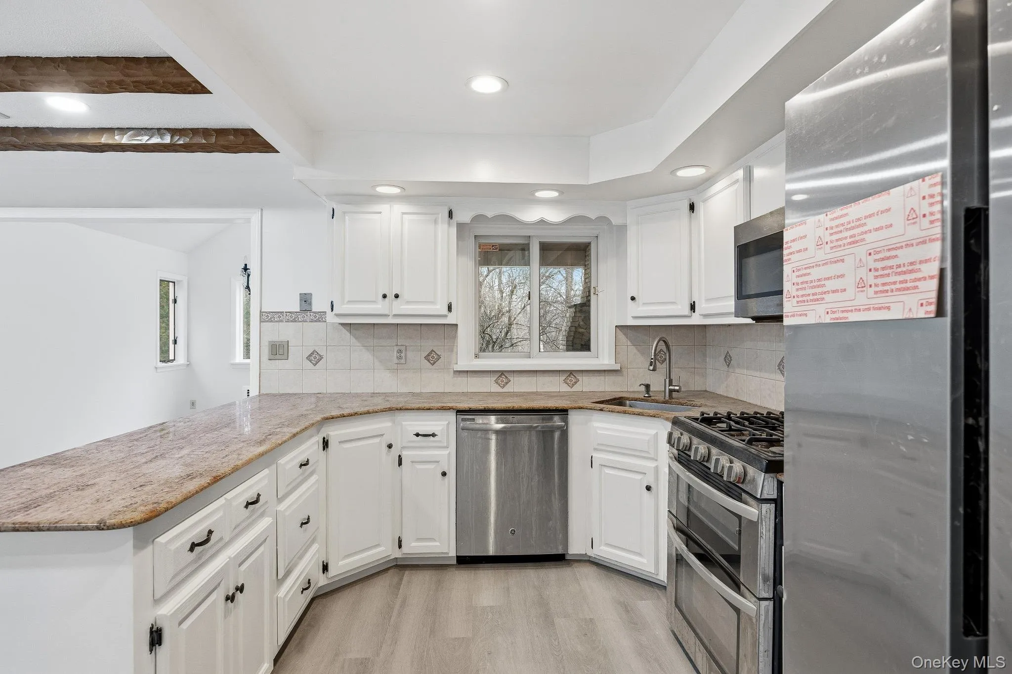 Kitchen with appliances with stainless steel finishes, tasteful backsplash, white cabinets, and light stone countertops Kitchen with appliances with stainless steel finishes, tasteful backsplash, white cabinets, and light stone countertops