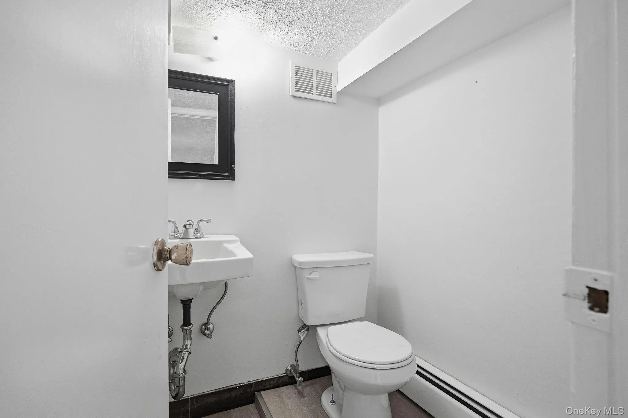 Half bath with a textured ceiling, a baseboard radiator, and wood finished floors Half bath with a textured ceiling, a baseboard radiator, and wood finished floors