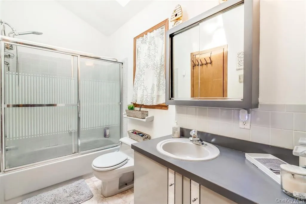 Bathroom with decorative backsplash, vanity, enclosed tub / shower combo, and vaulted ceiling Bathroom with decorative backsplash, vanity, enclosed tub / shower combo, and vaulted ceiling