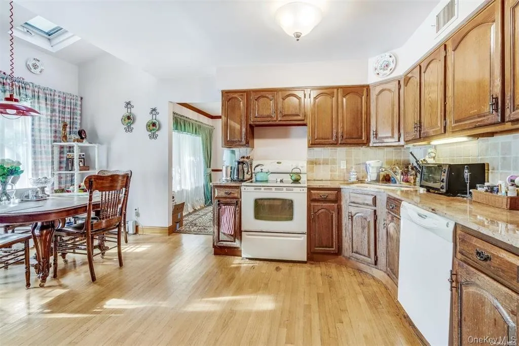 Kitchen featuring white appliances, a skylight, light wood-style flooring, backsplash, and brown cabinets Kitchen featuring white appliances, a skylight, light wood-style flooring, backsplash, and brown cabinets