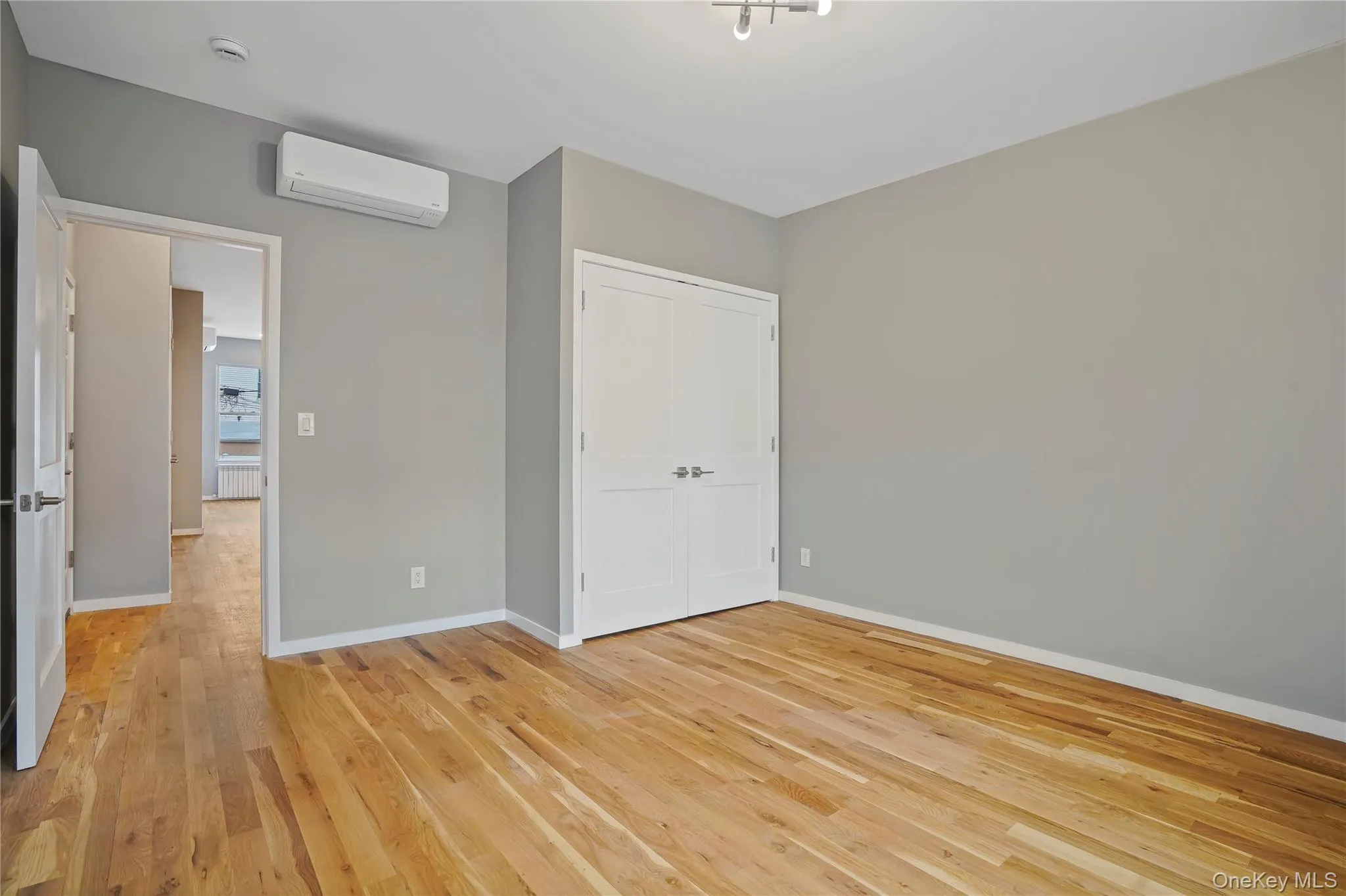 Unfurnished bedroom featuring light wood-style floors, a wall mounted air conditioner, and a closet Unfurnished bedroom featuring light wood-style floors, a wall mounted air conditioner, and a closet