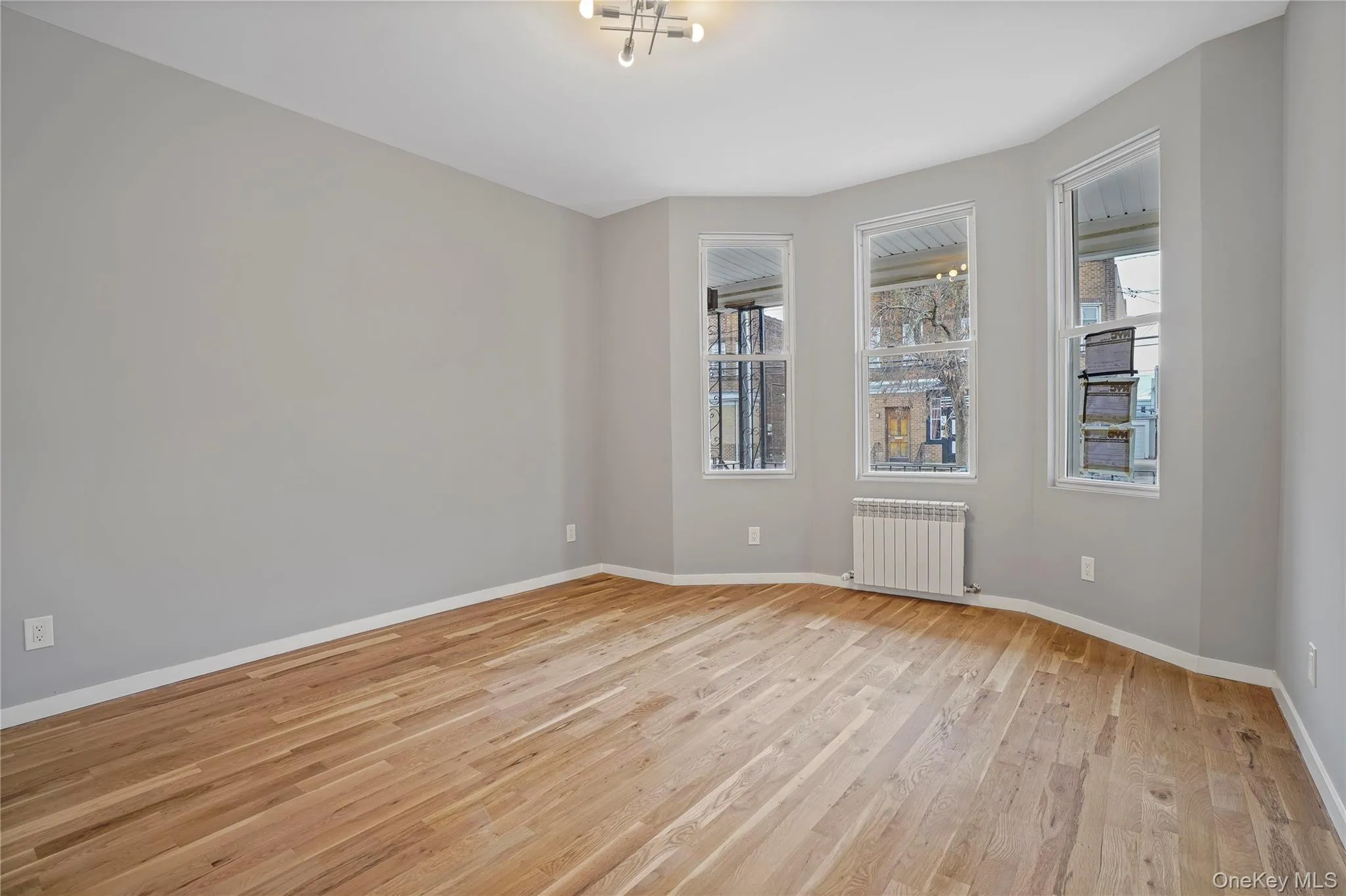 Unfurnished room with light wood-style flooring, plenty of natural light, and radiator heating unit Unfurnished room with light wood-style flooring, plenty of natural light, and radiator heating unit