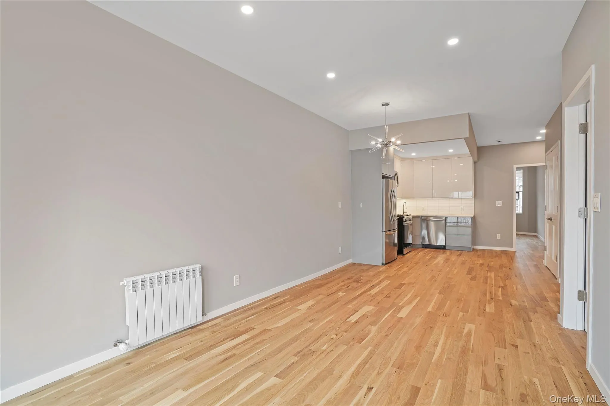 Unfurnished living room with radiator, recessed lighting, light wood finished floors, and a chandelier Unfurnished living room with radiator, recessed lighting, light wood finished floors, and a chandelier