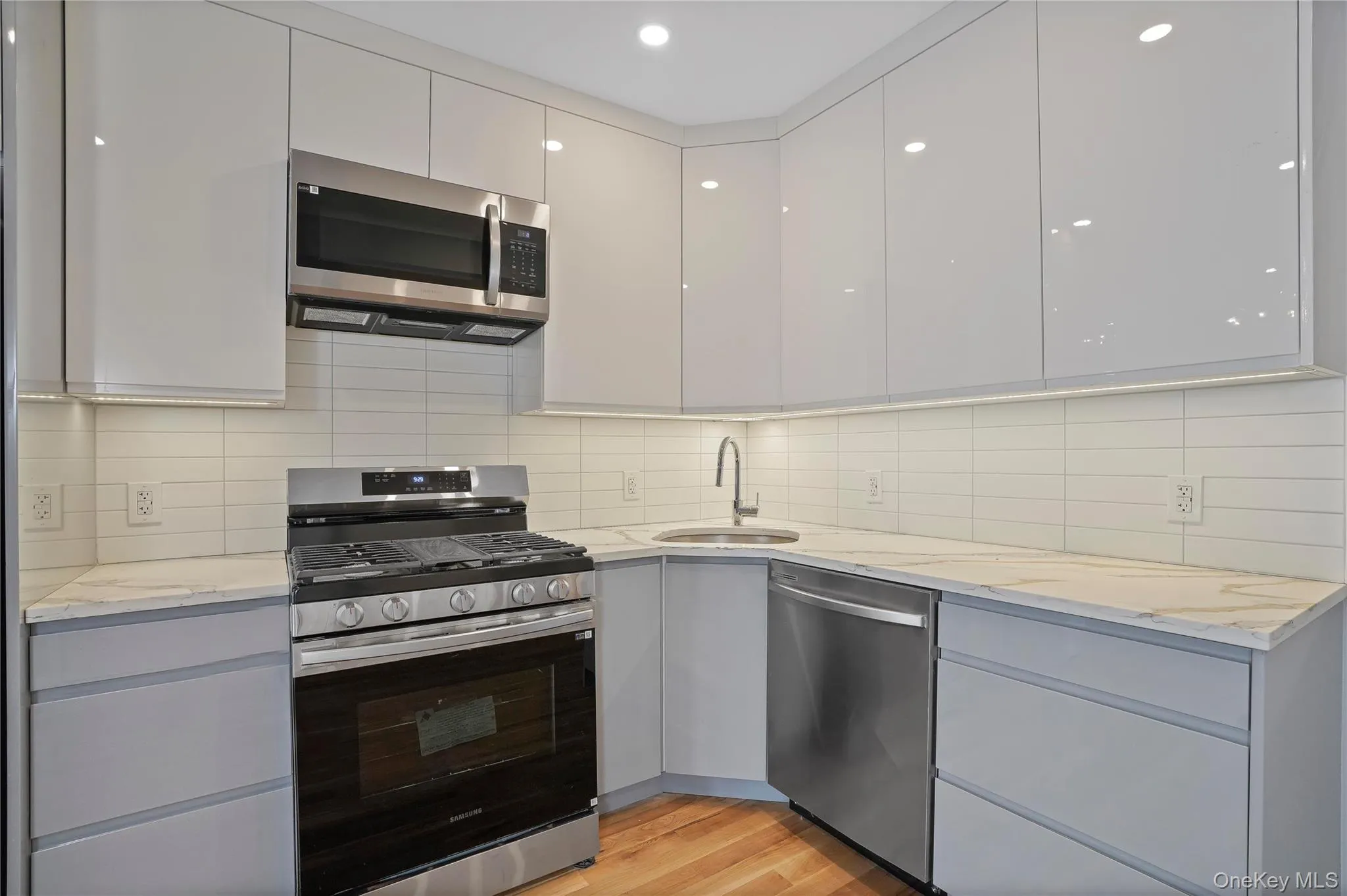 Kitchen with appliances with stainless steel finishes, gray cabinetry, light stone counters, and decorative backsplash Kitchen with appliances with stainless steel finishes, gray cabinetry, light stone counters, and decorative backsplash