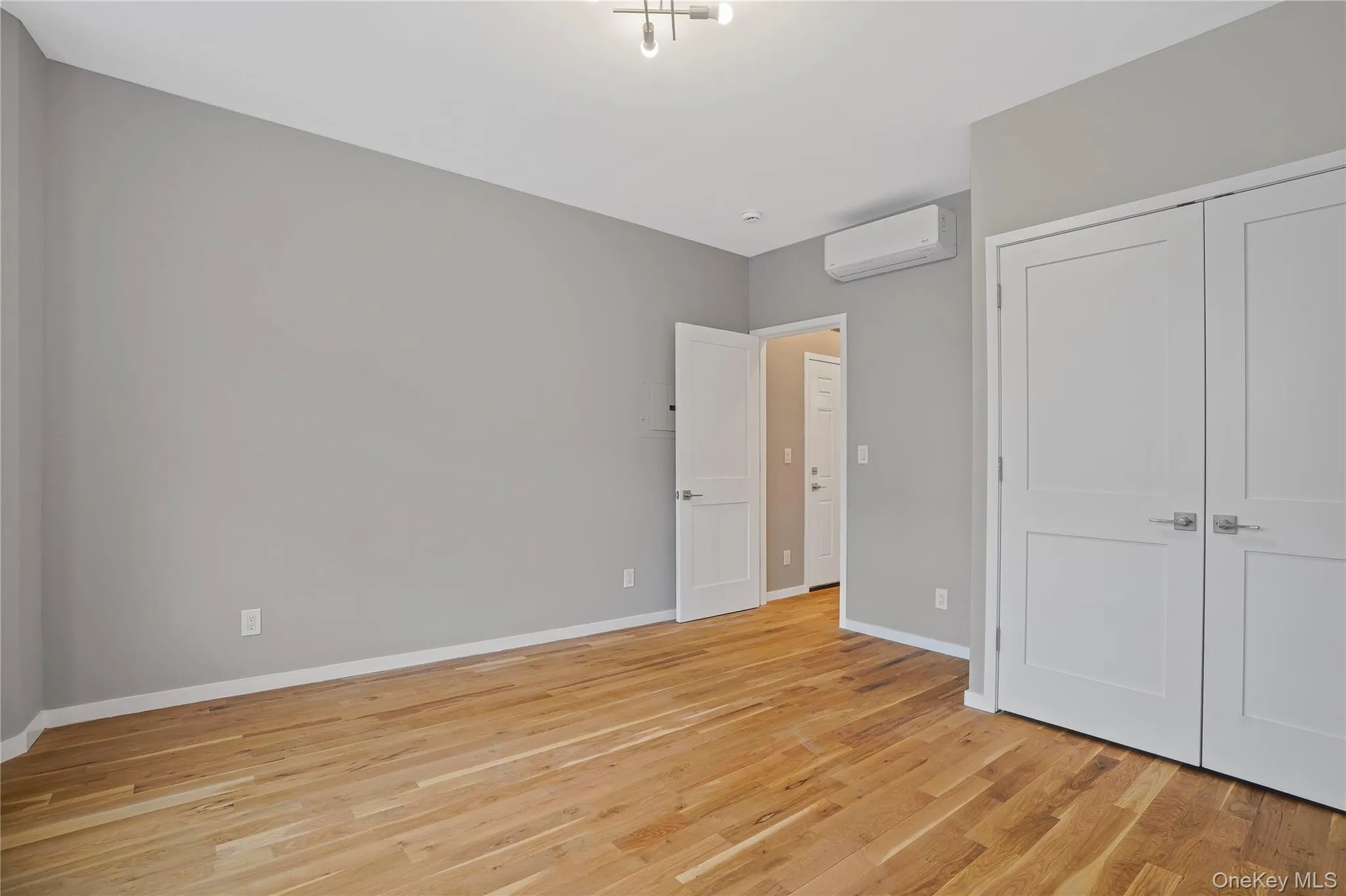 Unfurnished bedroom with light wood-style flooring, a wall unit AC, and a closet Unfurnished bedroom with light wood-style flooring, a wall unit AC, and a closet