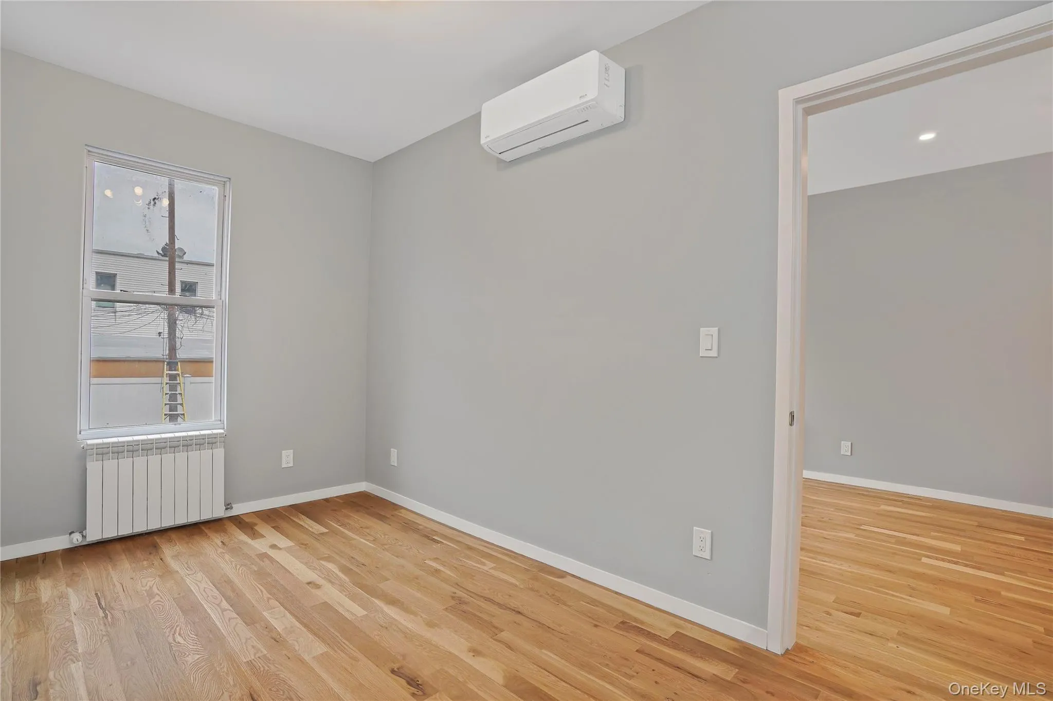 Unfurnished room featuring radiator heating unit, light wood finished floors, and an AC wall unit Unfurnished room featuring radiator heating unit, light wood finished floors, and an AC wall unit