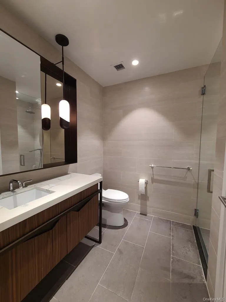 Bathroom featuring tile walls, a stall shower, vanity, recessed lighting, and light tile patterned floors Bathroom featuring tile walls, a stall shower, vanity, recessed lighting, and light tile patterned floors