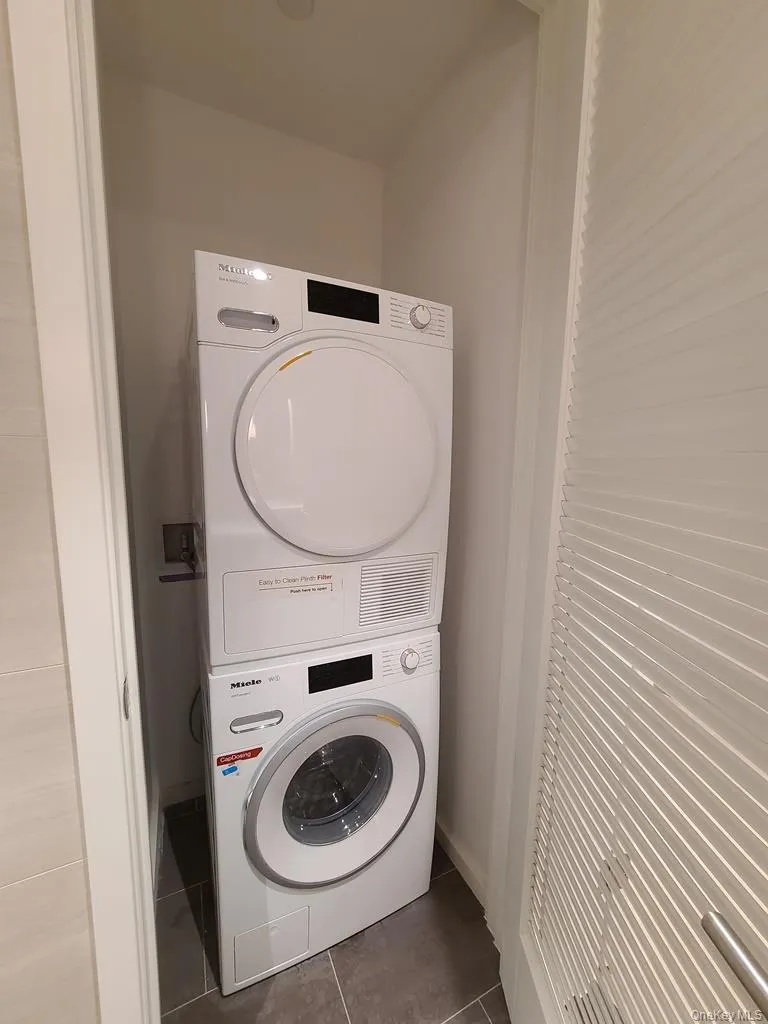 Washroom featuring dark tile patterned floors and stacked washer / dryer Washroom featuring dark tile patterned floors and stacked washer / dryer