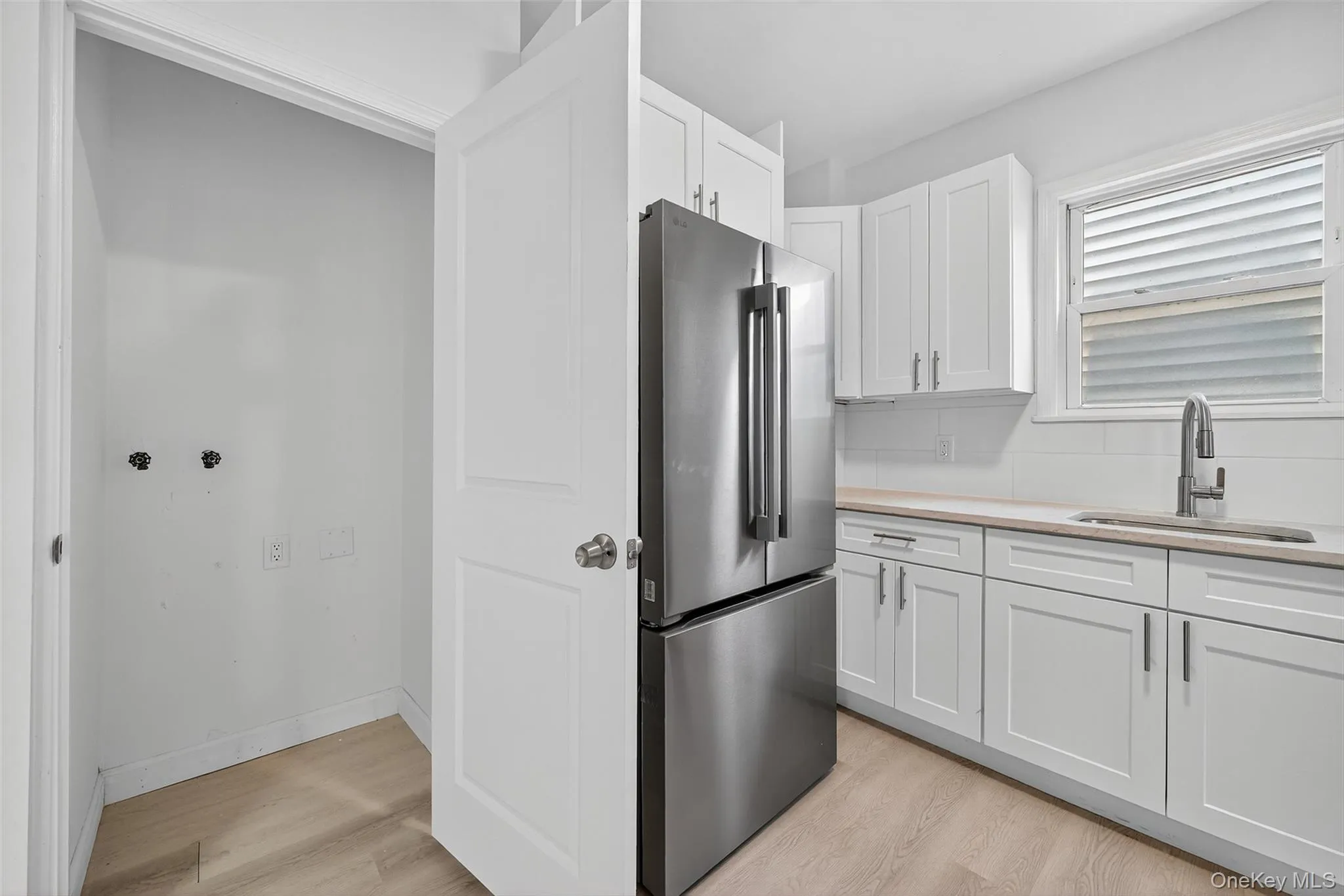 Kitchen with freestanding refrigerator, white cabinets, light wood-style floors, and light stone counters Kitchen with freestanding refrigerator, white cabinets, light wood-style floors, and light stone counters
