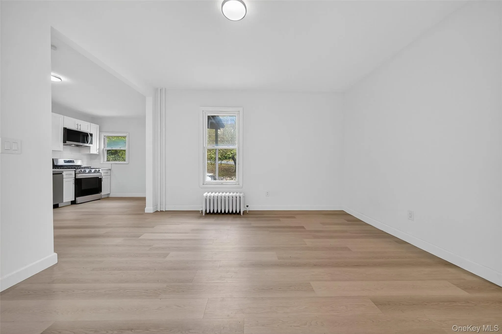 Unfurnished living room featuring light wood-type flooring and radiator Unfurnished living room featuring light wood-type flooring and radiator