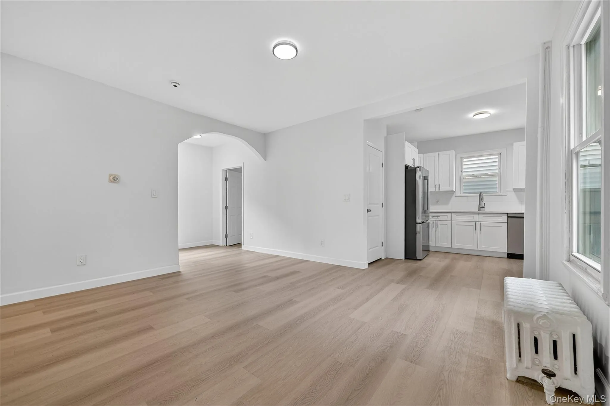 Unfurnished living room with radiator heating unit, arched walkways, and light wood-style floors Unfurnished living room with radiator heating unit, arched walkways, and light wood-style floors