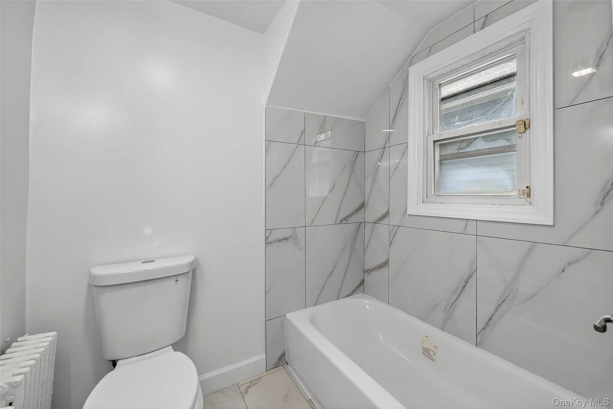 Full bathroom with radiator, lofted ceiling, tub / shower combination, and marble finish floors Full bathroom with radiator, lofted ceiling, tub / shower combination, and marble finish floors