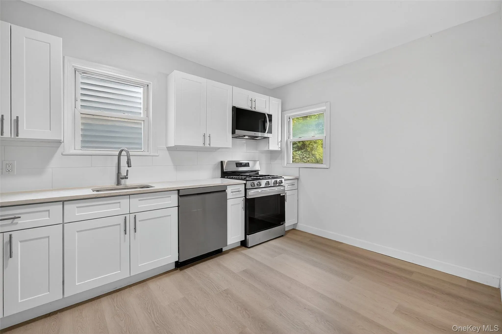 Kitchen featuring white cabinetry, stainless steel appliances, decorative backsplash, light wood finished floors, and light stone counters Kitchen featuring white cabinetry, stainless steel appliances, decorative backsplash, light wood finished floors, and light stone counters