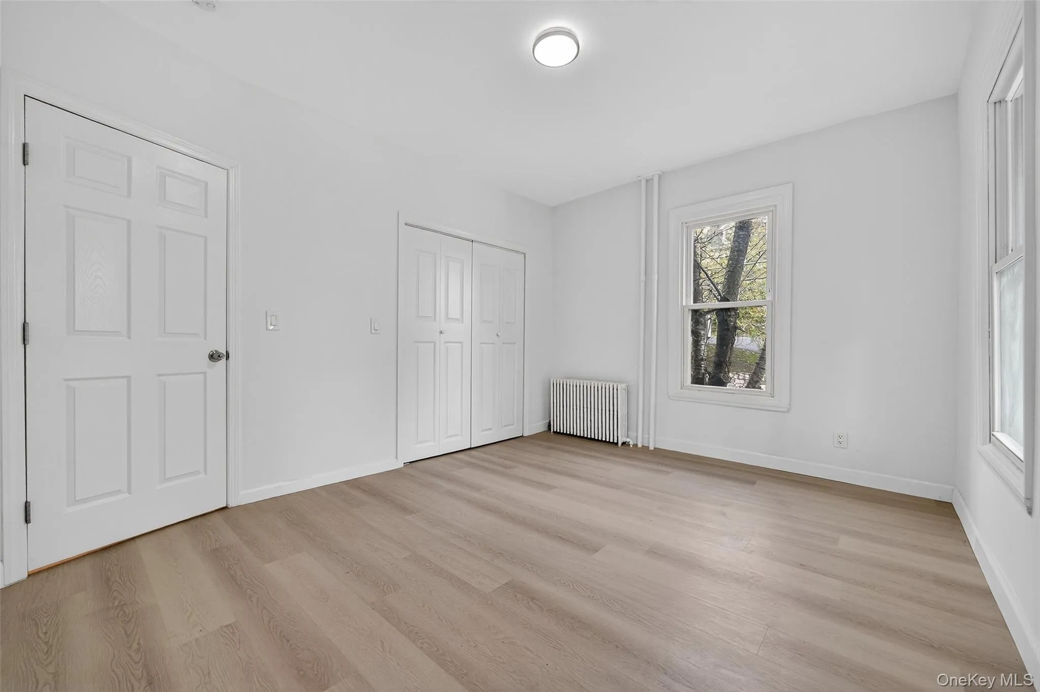 Unfurnished bedroom featuring radiator, light wood-style floors, and a closet Unfurnished bedroom featuring radiator, light wood-style floors, and a closet