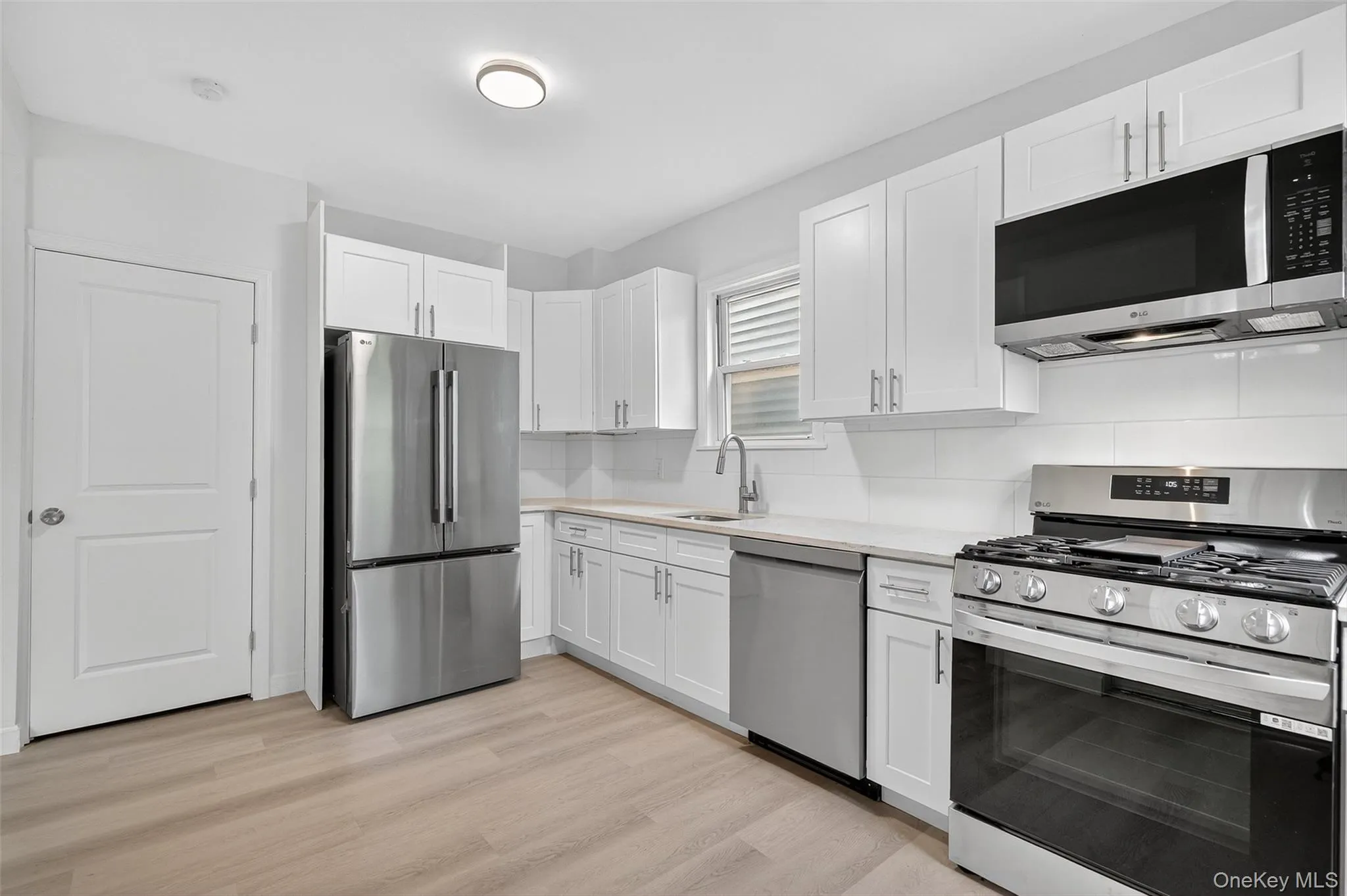 Kitchen with stainless steel appliances, white cabinetry, backsplash, light wood finished floors, and light stone counters Kitchen with stainless steel appliances, white cabinetry, backsplash, light wood finished floors, and light stone counters