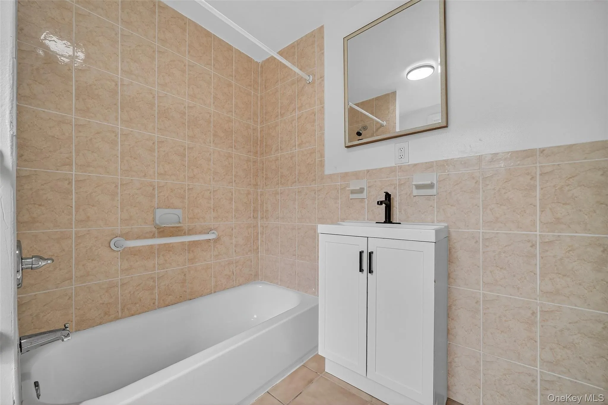 Bathroom with shower / bathtub combination, vanity, light tile patterned floors, and tile walls Bathroom with shower / bathtub combination, vanity, light tile patterned floors, and tile walls
