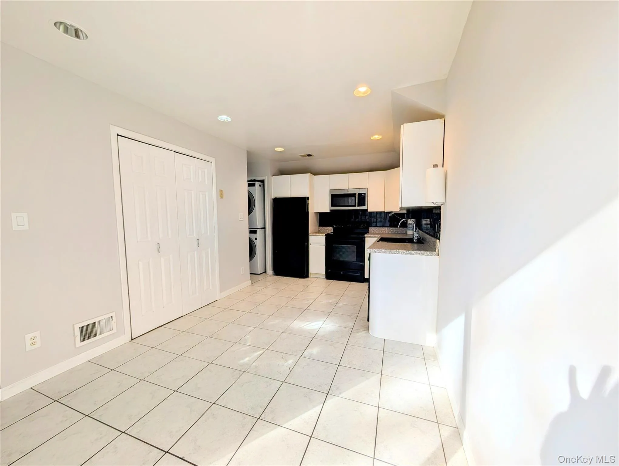 Kitchen with light tile patterned floors, white cabinetry, black appliances, estacked washer and dryer, and backsplash Kitchen with light tile patterned floors, white cabinetry, black appliances, estacked washer and dryer, and backsplash