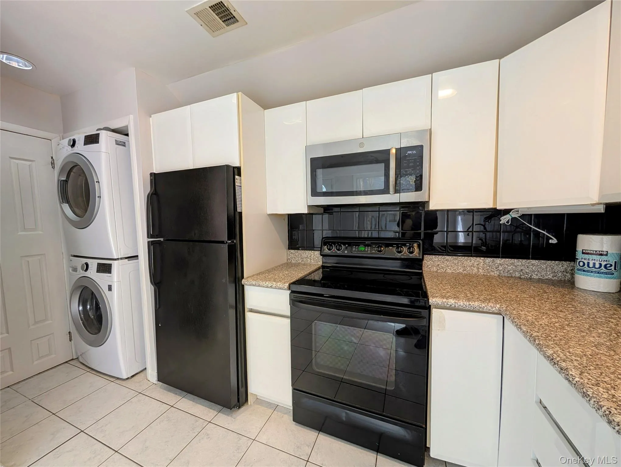 Kitchen with black appliances, white cabinetry, tasteful backsplash, light tile patterned floors, and light stone counters Kitchen with black appliances, white cabinetry, tasteful backsplash, light tile patterned floors, and light stone counters
