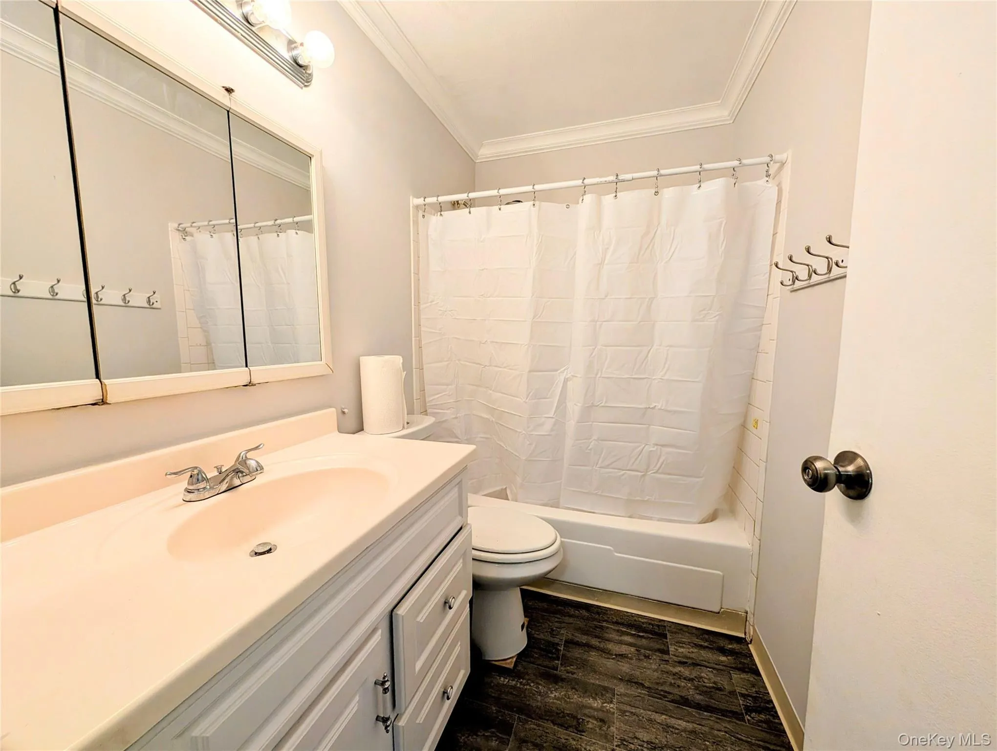 Full bathroom featuring ornamental molding, dark wood-style flooring, vanity, and shower / bathtub combination with curtain Full bathroom featuring ornamental molding, dark wood-style flooring, vanity, and shower / bathtub combination with curtain