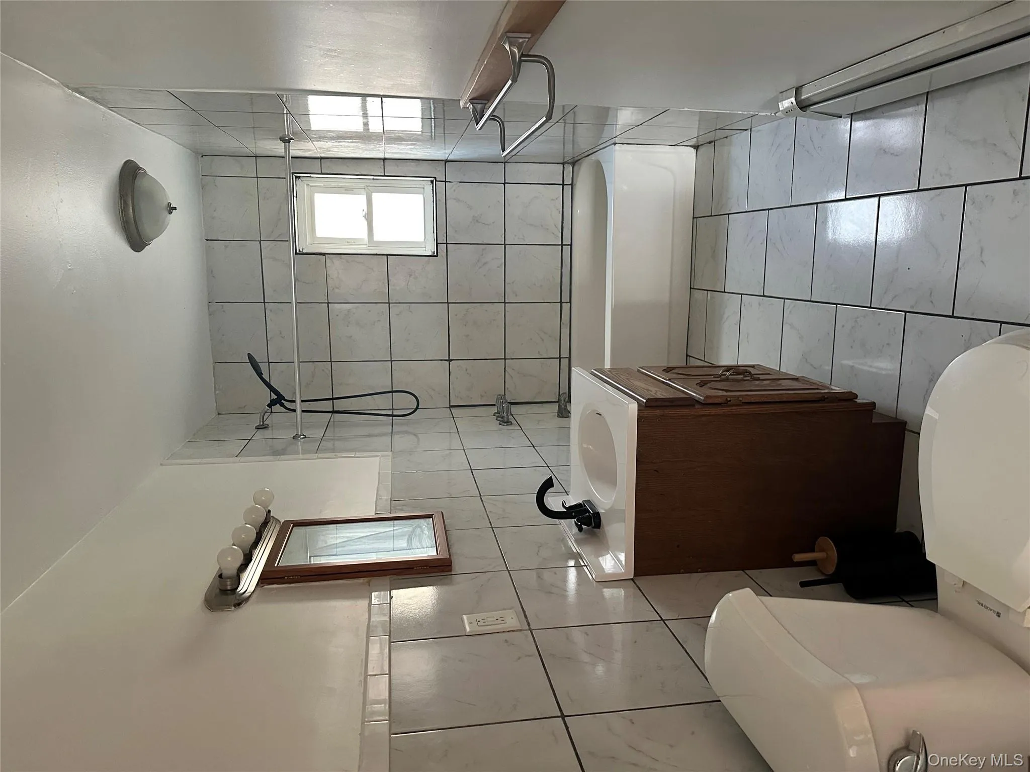 Full bathroom with vanity, tile walls, shower / bathtub combination, light marble finish flooring, and a baseboard heating unit Full bathroom with vanity, tile walls, shower / bathtub combination, light marble finish flooring, and a baseboard heating unit