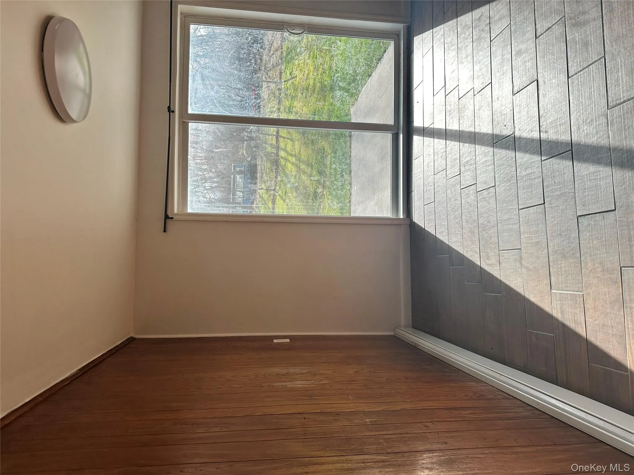 Empty room featuring a baseboard heating unit, light wood-type flooring, and wood walls Empty room featuring a baseboard heating unit, light wood-type flooring, and wood walls