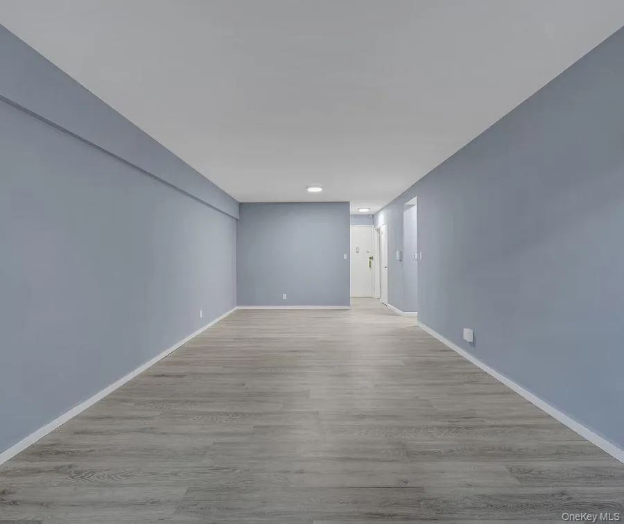 View from the far end of the living and dining area facing the unit's front entrance with light wood-style flooring and baseboards View from the far end of the living and dining area facing the unit's front entrance with light wood-style flooring and baseboards