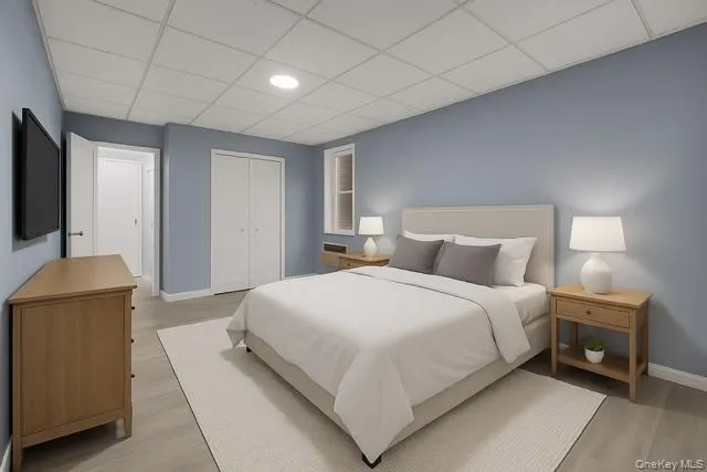 Virtually Staged spacious bedroom featuring a drop ceiling, light wood-style flooring, and a closet Virtually Staged spacious bedroom featuring a drop ceiling, light wood-style flooring, and a closet