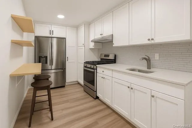 Virtually Staged kitchen featuring stainless steel appliances, white cabinetry, light wood-style flooring, under cabinet range hood, and backsplash Virtually Staged kitchen featuring stainless steel appliances, white cabinetry, light wood-style flooring, under cabinet range hood, and backsplash