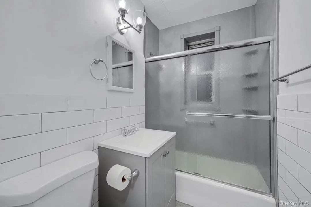Bathroom featuring shower / bath combination with glass door, vanity, and subway tile walls Bathroom featuring shower / bath combination with glass door, vanity, and subway tile walls