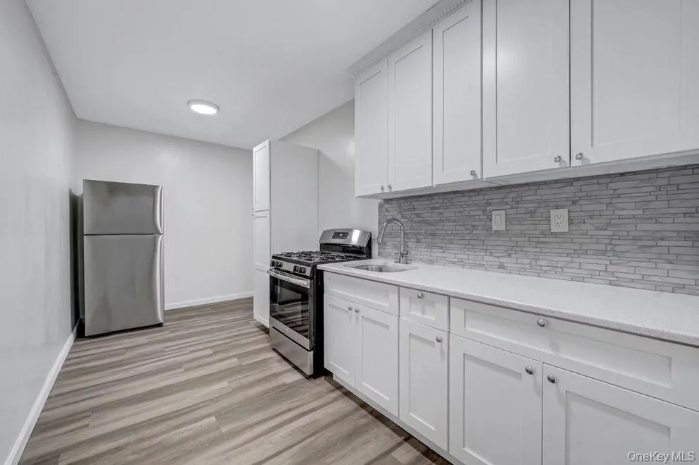 Kitchen with appliances with stainless steel finishes, light wood-style flooring, backsplash, and white shaker cabinets Kitchen with appliances with stainless steel finishes, light wood-style flooring, backsplash, and white shaker cabinets