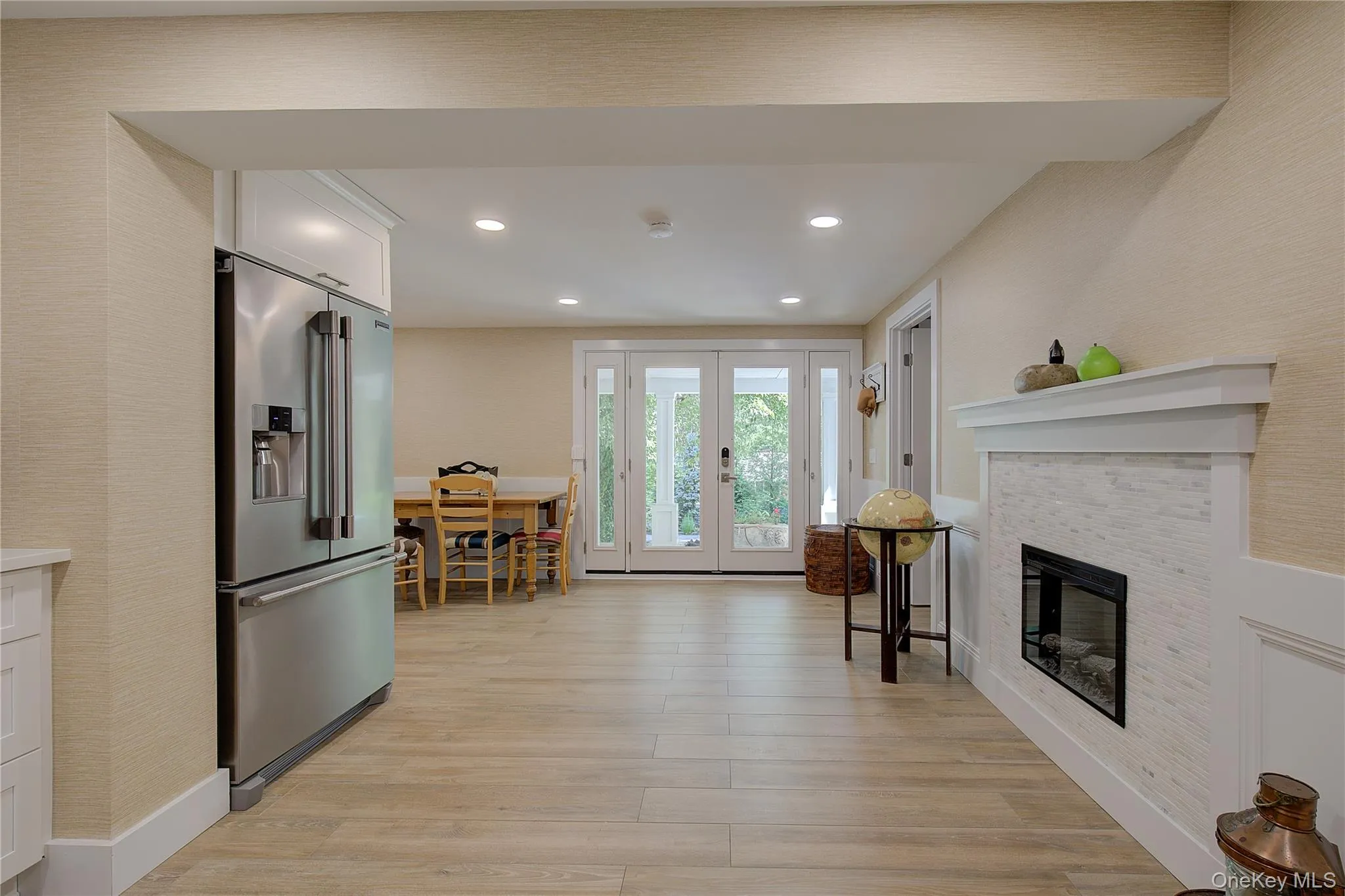 Kitchen featuring white cabinets, high end fridge, light wood-style flooring, a tiled fireplace, and recessed lighting Kitchen featuring white cabinets, high end fridge, light wood-style flooring, a tiled fireplace, and recessed lighting