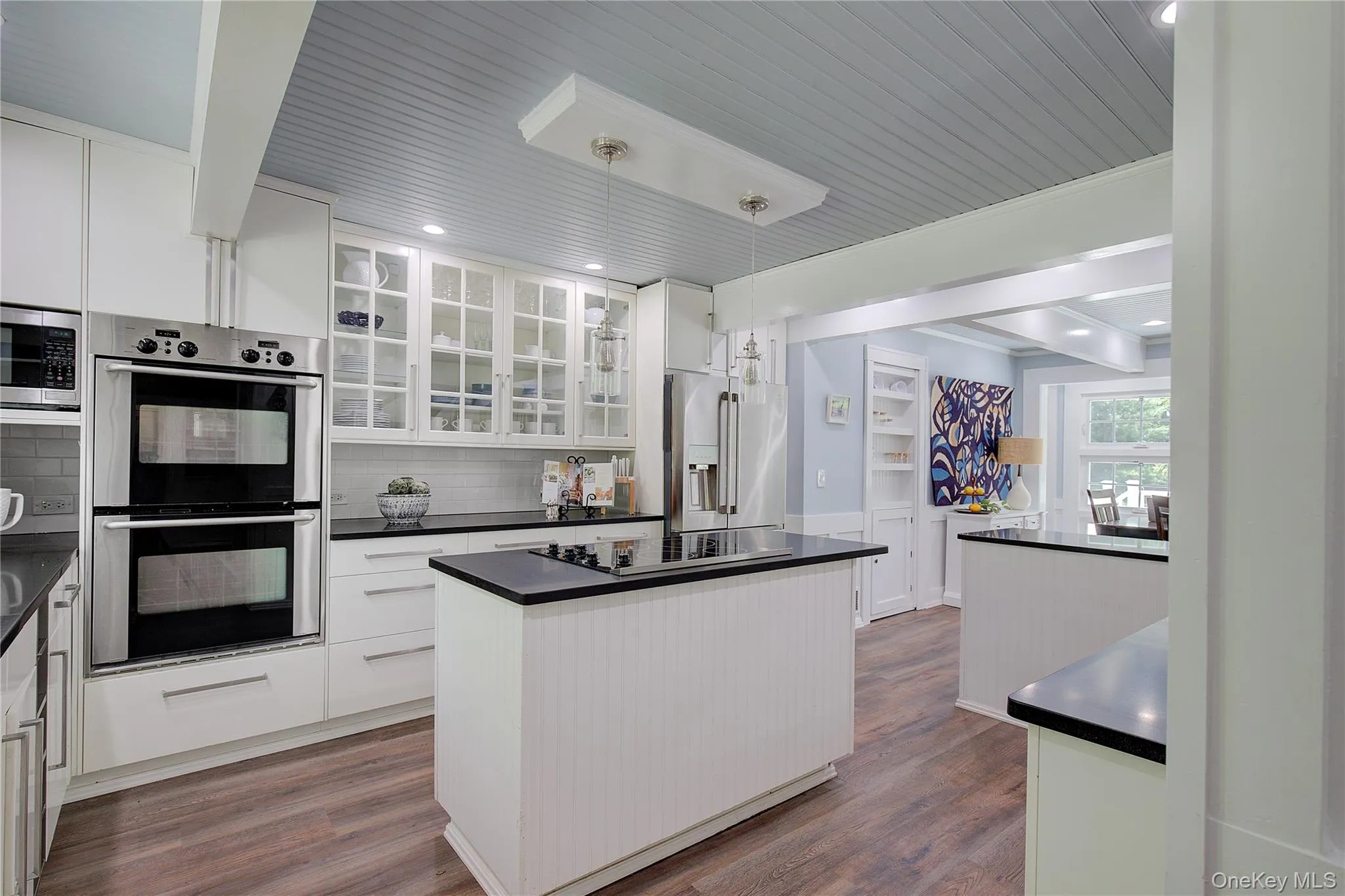 Kitchen with appliances with stainless steel finishes, dark wood-style flooring, white cabinetry, decorative backsplash, and hanging light fixtures Kitchen with appliances with stainless steel finishes, dark wood-style flooring, white cabinetry, decorative backsplash, and hanging light fixtures