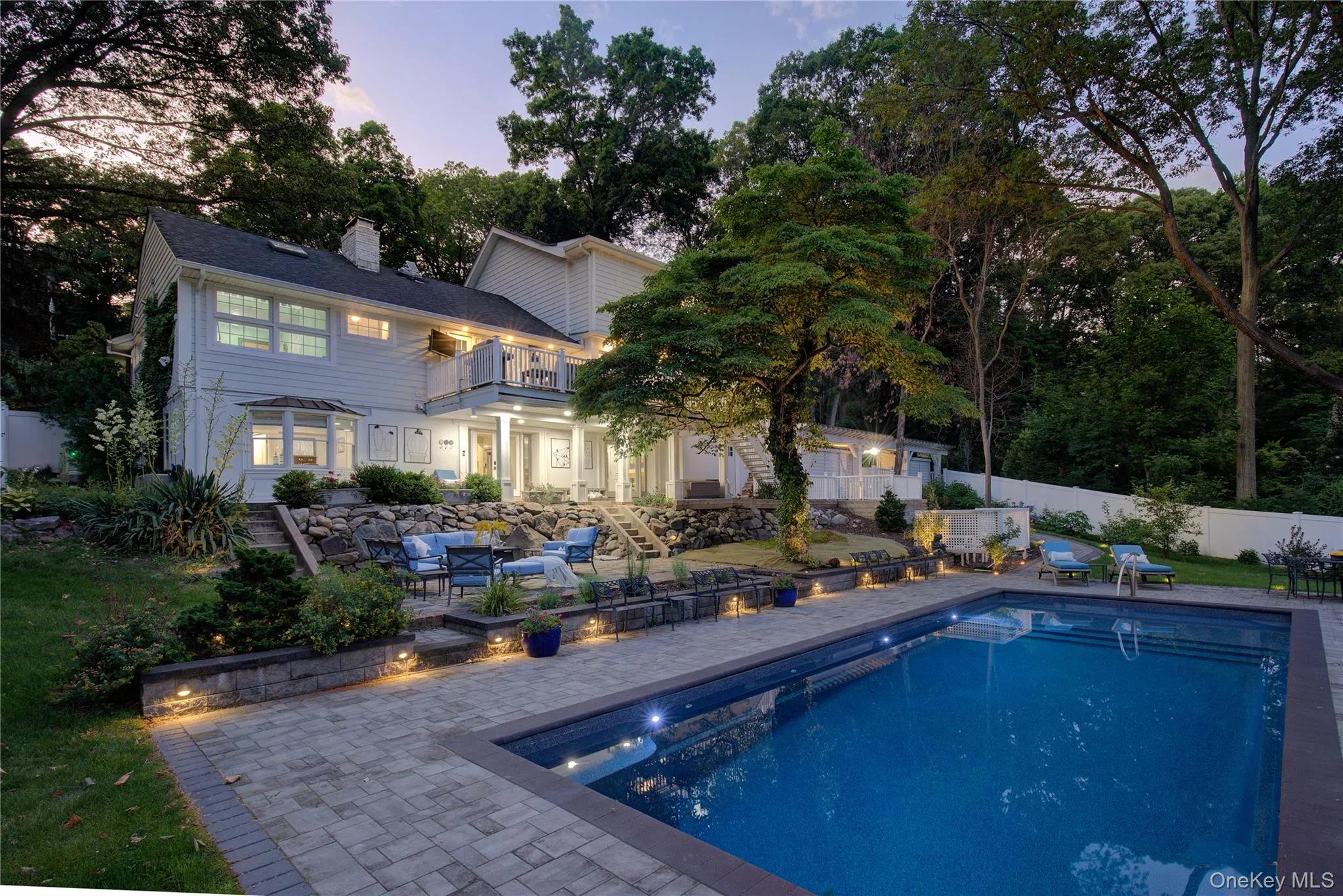Back of property at dusk featuring a patio, a balcony, a fenced backyard, an outdoor living space, and a chimney Back of property at dusk featuring a patio, a balcony, a fenced backyard, an outdoor living space, and a chimney