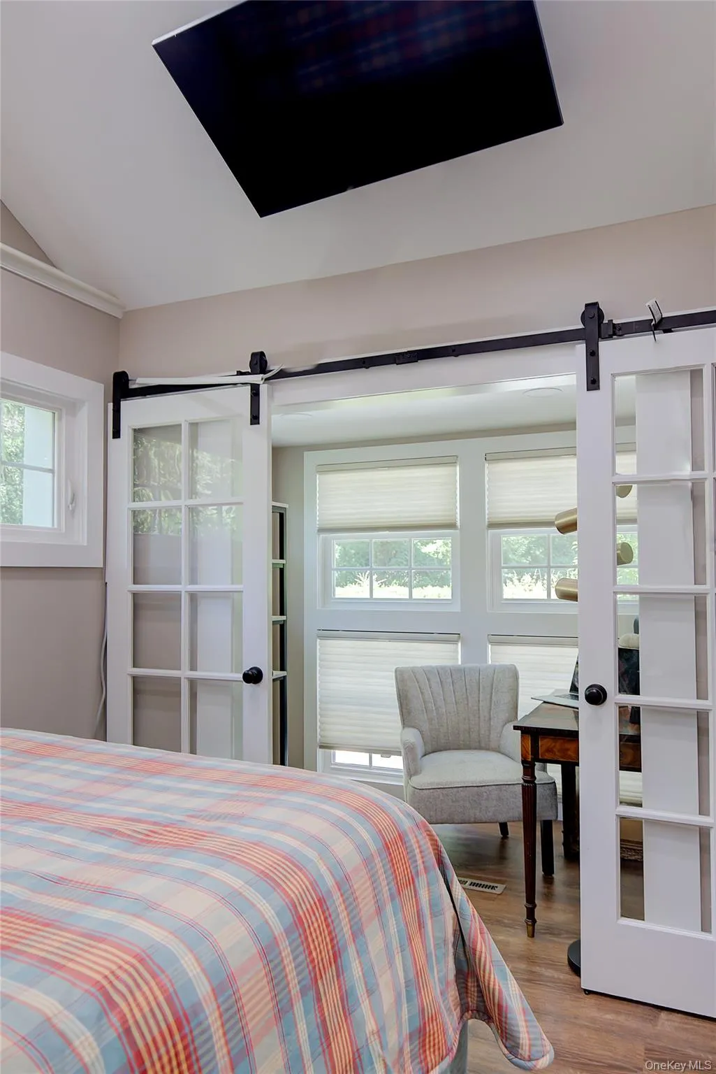 Bedroom with a barn door, multiple windows, wood finished floors, and vaulted ceiling Bedroom with a barn door, multiple windows, wood finished floors, and vaulted ceiling
