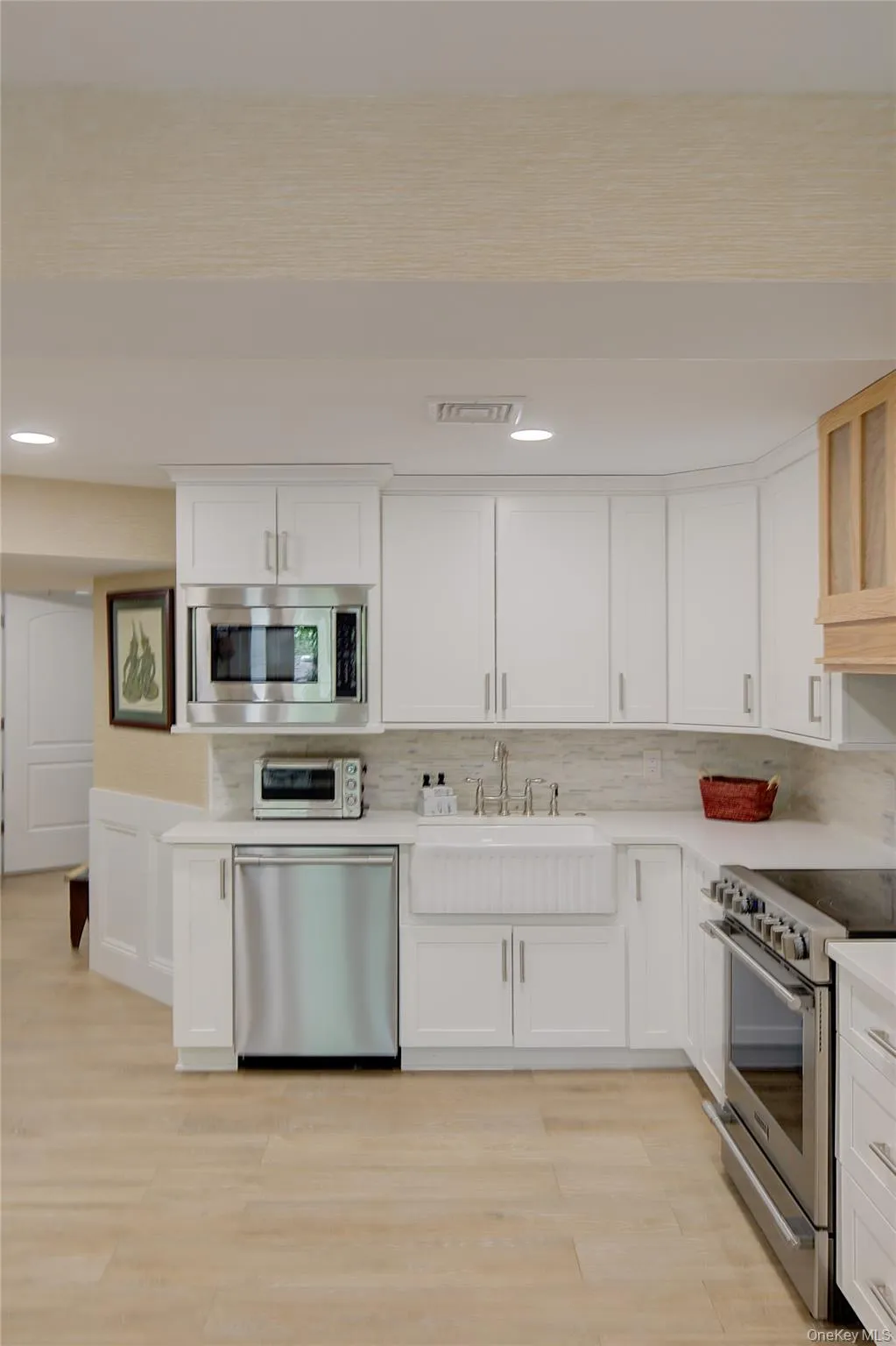 Kitchen featuring appliances with stainless steel finishes, white cabinetry, decorative backsplash, recessed lighting, and light wood finished floors Kitchen featuring appliances with stainless steel finishes, white cabinetry, decorative backsplash, recessed lighting, and light wood finished floors