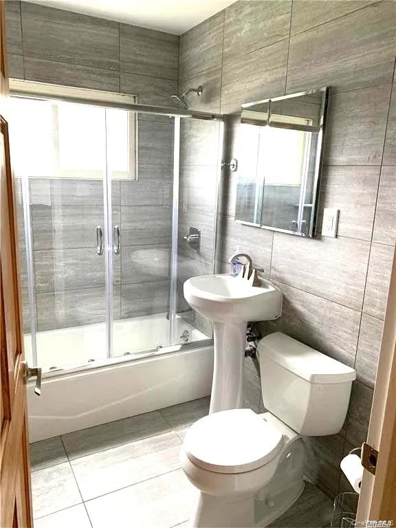 Full bath featuring bath / shower combo with glass door, tile walls, and light tile patterned floors Full bath featuring bath / shower combo with glass door, tile walls, and light tile patterned floors