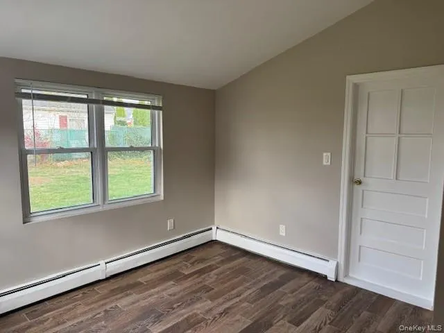 Spare room featuring dark wood-style floors, lofted ceiling, and a baseboard radiator Spare room featuring dark wood-style floors, lofted ceiling, and a baseboard radiator