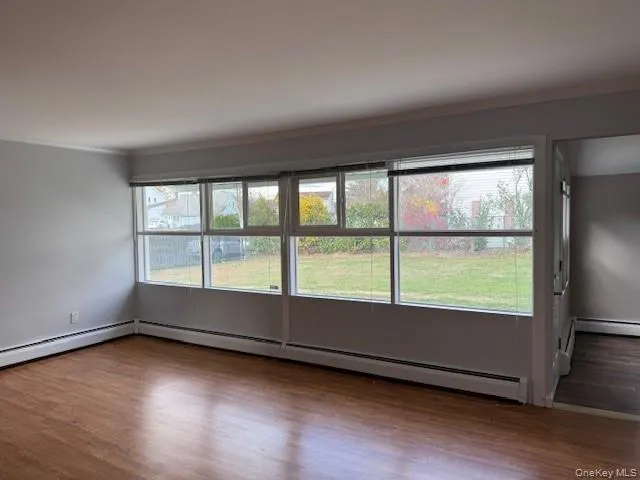 Unfurnished room featuring crown molding, a baseboard heating unit, and dark wood-style floors Unfurnished room featuring crown molding, a baseboard heating unit, and dark wood-style floors