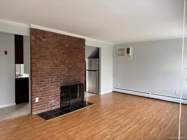 Unfurnished living room featuring ornamental molding, a brick fireplace, light wood-type flooring, and a baseboard radiator Unfurnished living room featuring ornamental molding, a brick fireplace, light wood-type flooring, and a baseboard radiator