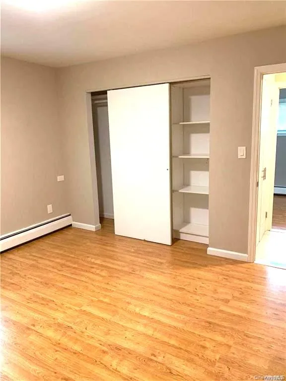 Unfurnished bedroom featuring light wood-style floors, a baseboard heating unit, a closet, and a baseboard radiator Unfurnished bedroom featuring light wood-style floors, a baseboard heating unit, a closet, and a baseboard radiator