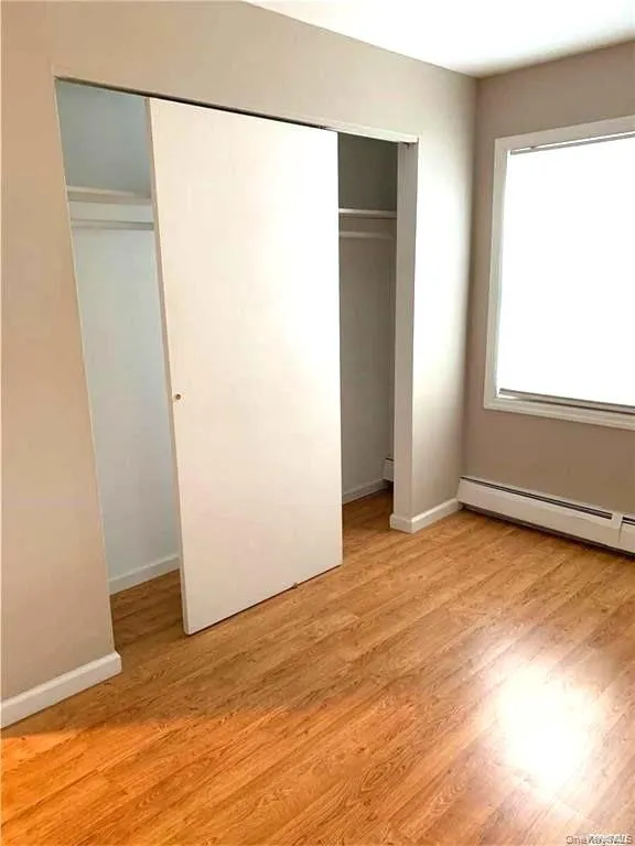 Unfurnished bedroom with a baseboard heating unit, light wood-type flooring, and a closet Unfurnished bedroom with a baseboard heating unit, light wood-type flooring, and a closet