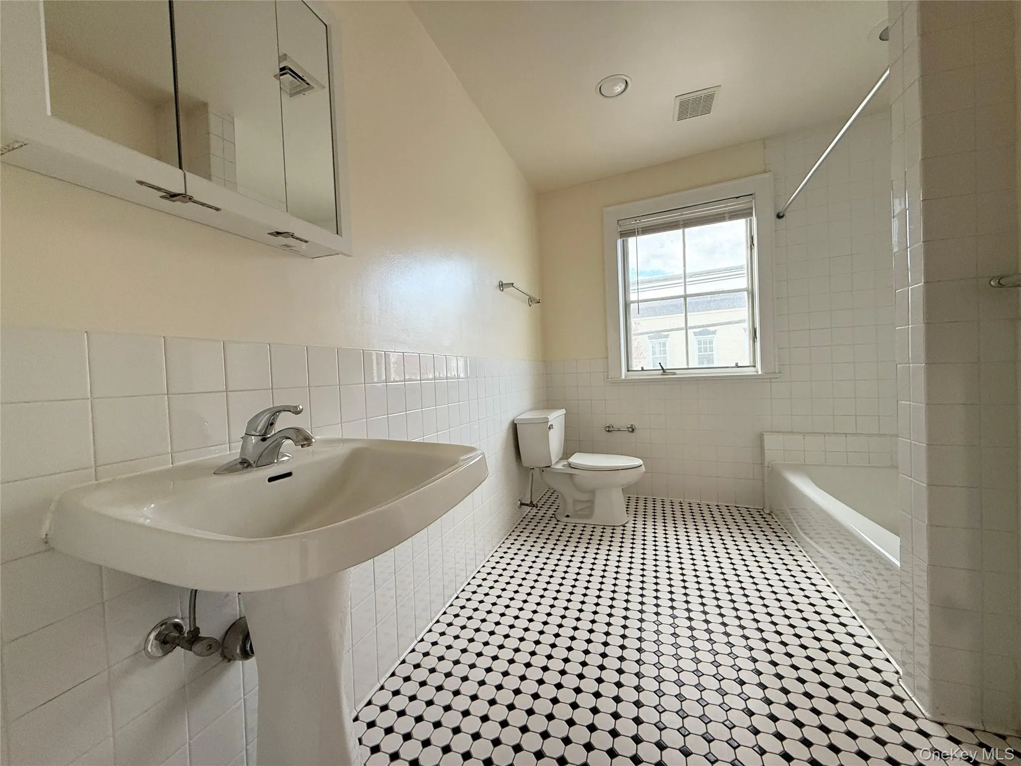 Full bathroom with tile walls, washtub / shower combination, tile patterned floors, and wainscoting Full bathroom with tile walls, washtub / shower combination, tile patterned floors, and wainscoting