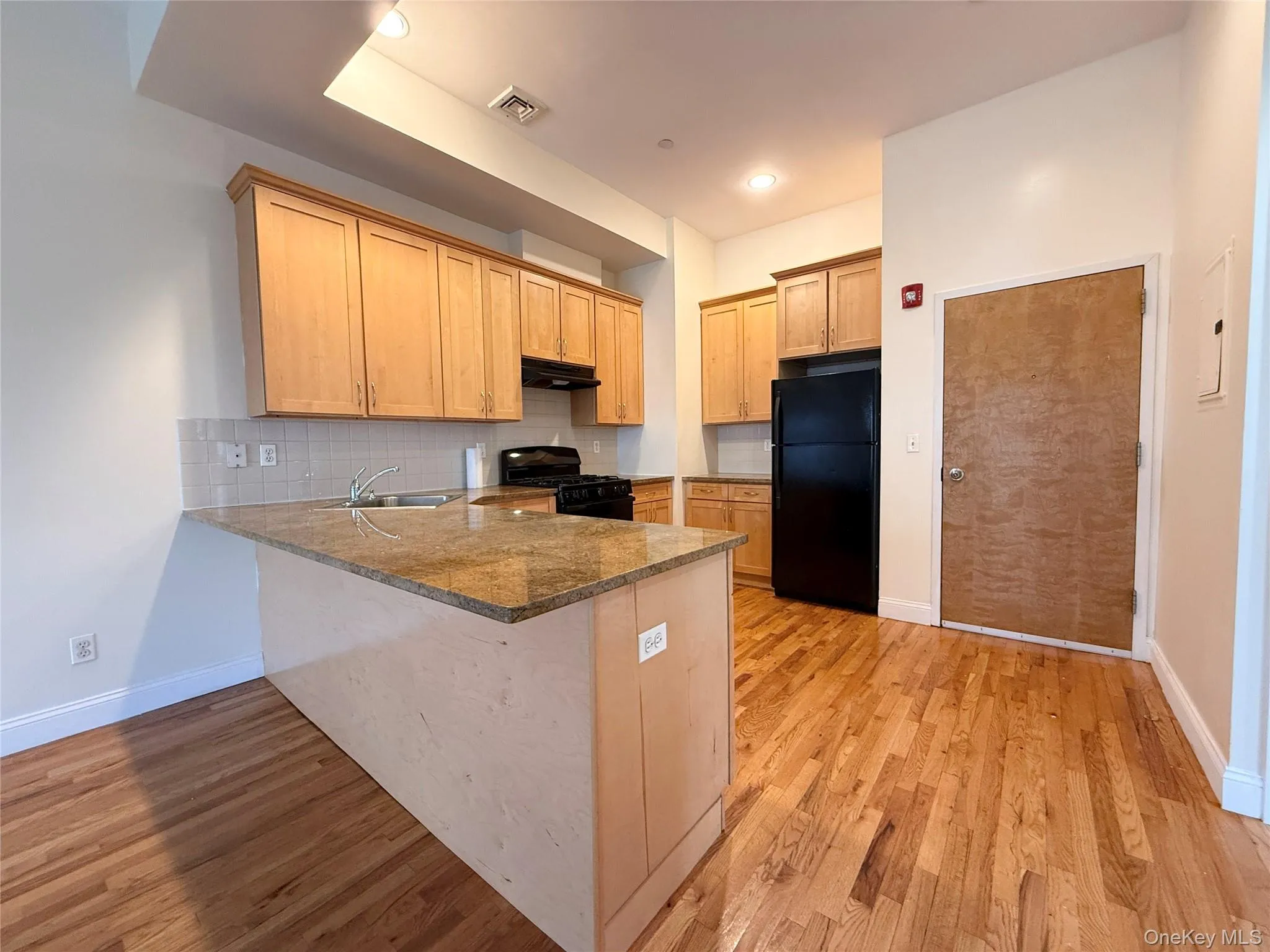 Kitchen with tasteful backsplash, a peninsula, black appliances, and light wood finished floors Kitchen with tasteful backsplash, a peninsula, black appliances, and light wood finished floors