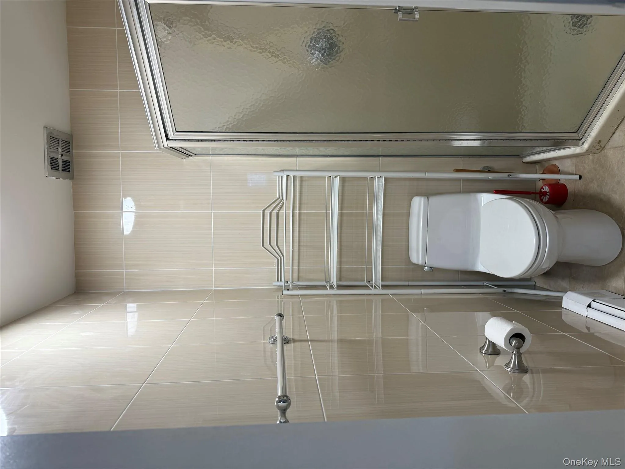 Bathroom with a shower stall, tile walls, a baseboard radiator, and light tile patterned flooring Bathroom with a shower stall, tile walls, a baseboard radiator, and light tile patterned flooring