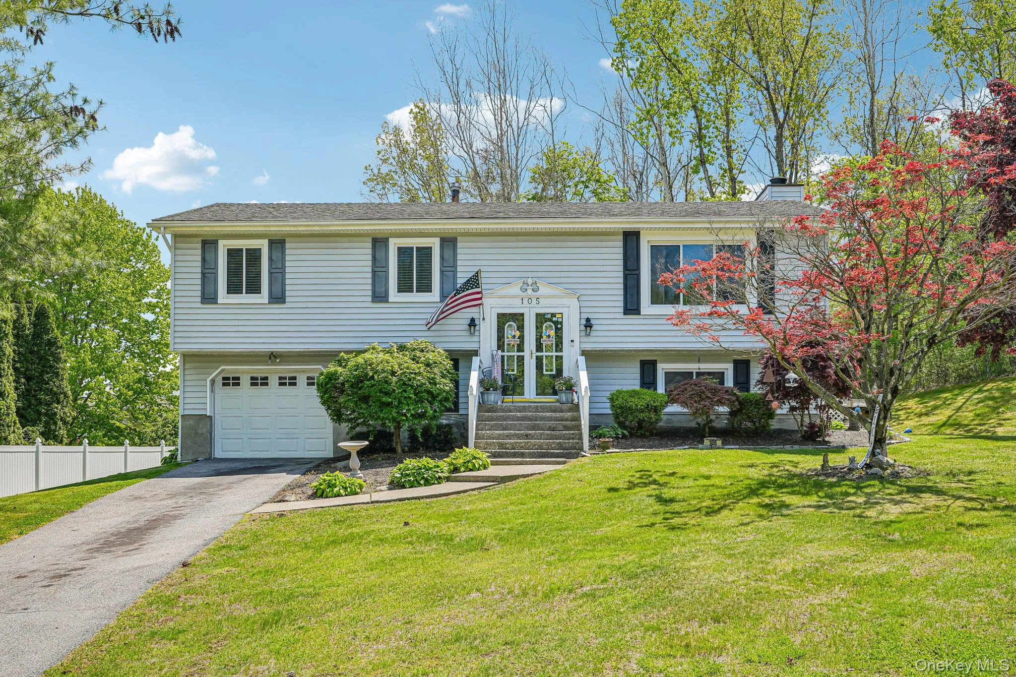 Split-level residence featuring light-colored siding, a prominent attached garage, and driveway. some photos may include virtually staged or digitally modified Split-level residence featuring light-colored siding, a prominent attached garage, and driveway. some photos may include virtually staged or digitally modified
