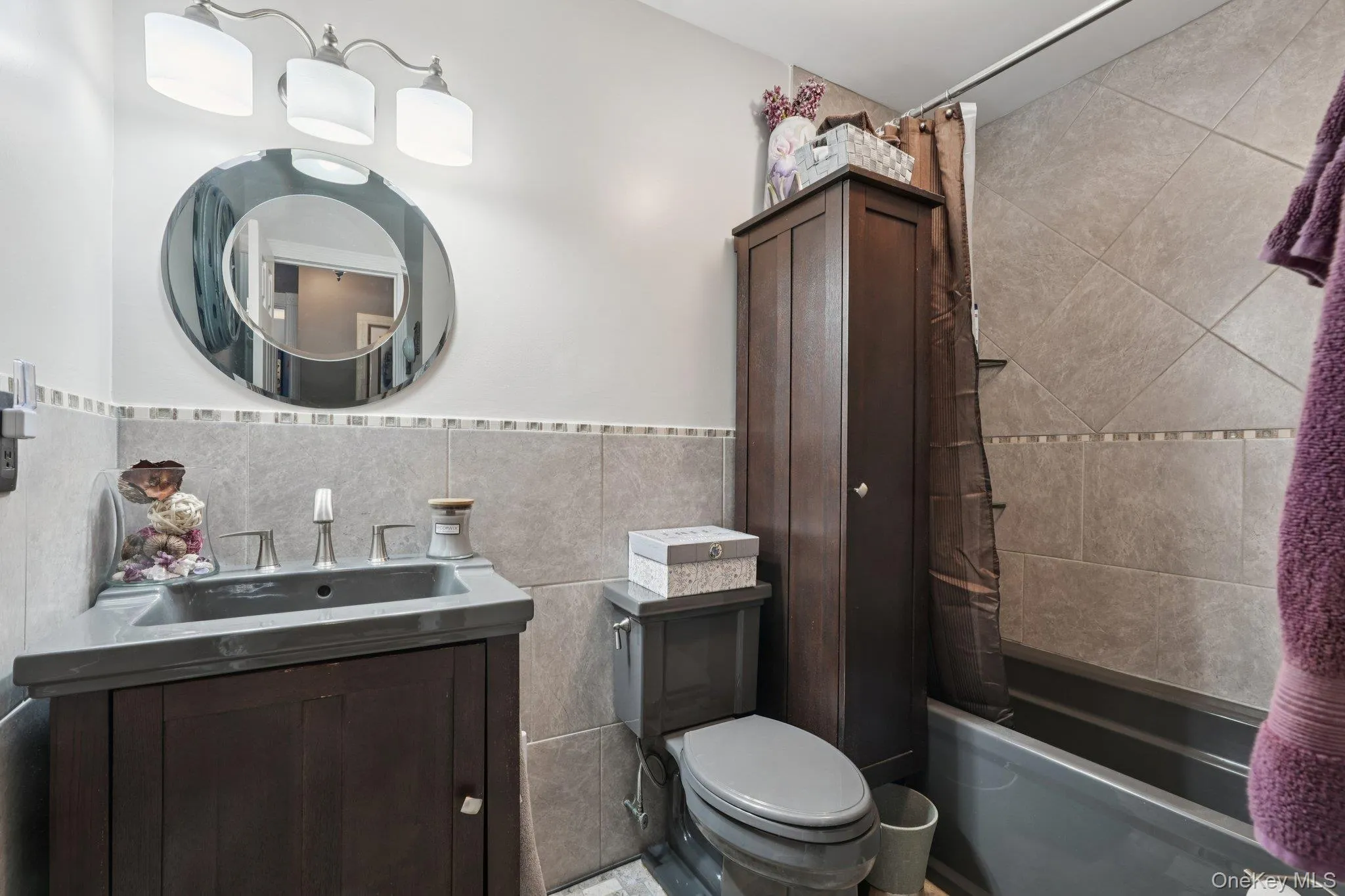 Full bathroom featuring tile walls, vanity, shower / bath combo, and a wainscoted wall. some photos may include virtually staged or digitally modified Full bathroom featuring tile walls, vanity, shower / bath combo, and a wainscoted wall. some photos may include virtually staged or digitally modified