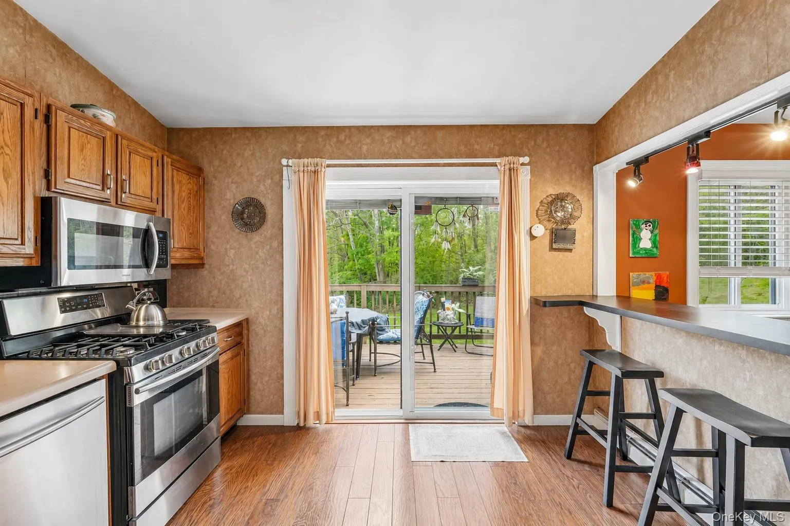 Eat-in kitchen featuring wood-finish flooring and stainless steel appliances. Digitally enhanced photo Eat-in kitchen featuring wood-finish flooring and stainless steel appliances. Digitally enhanced photo